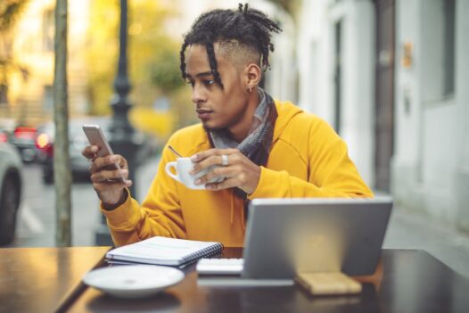 A young man uses an online payment method while sitting outside at a cafe.