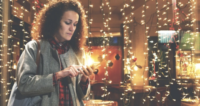 A woman shops on her phone using social commerce outside a brightly lit store