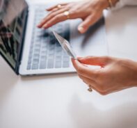 Woman Holds Credit Card While Shopping On Laptop And Wonders If Her Card Is PCI Compliant