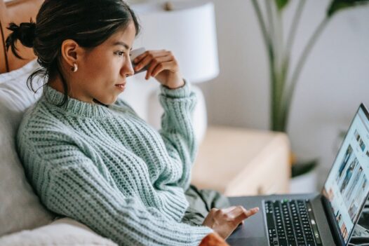 Woman in sweater holds her credit card while shopping on her laptop