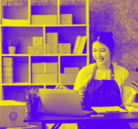 A Woman In An Apron Looking At A Computer And Holding A Notebook Represents Ecommercepayment Processing: A Comprehensive Guide For Merchants